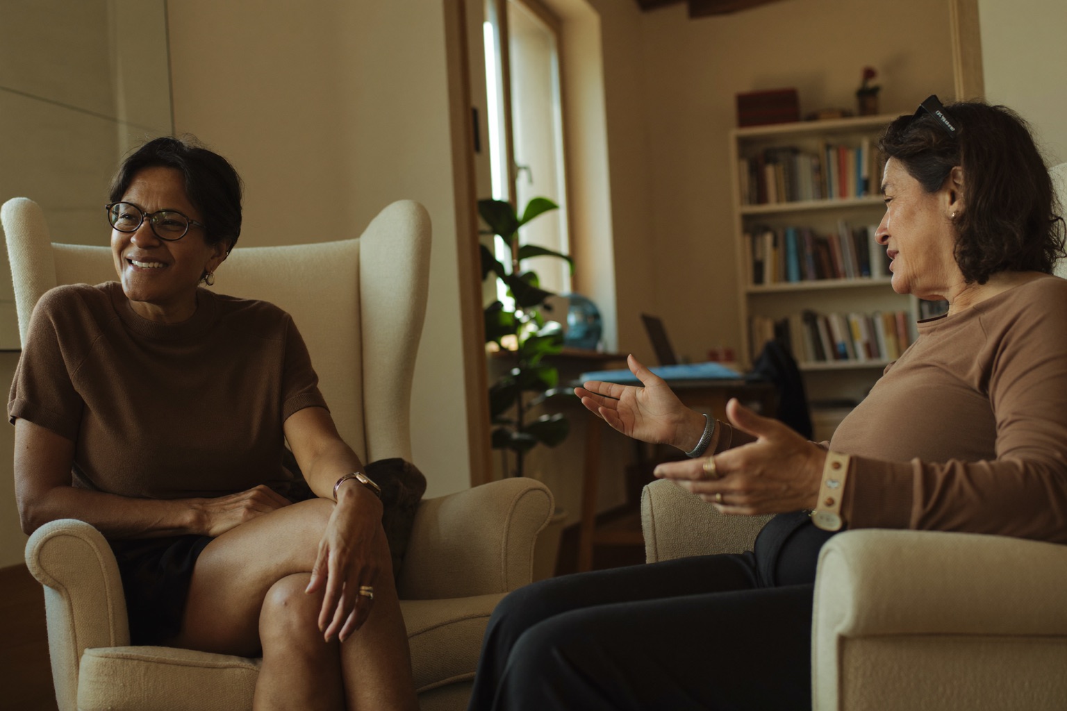 Two people in a relaxed conversation in armchairs in a bright, plainly furnished room